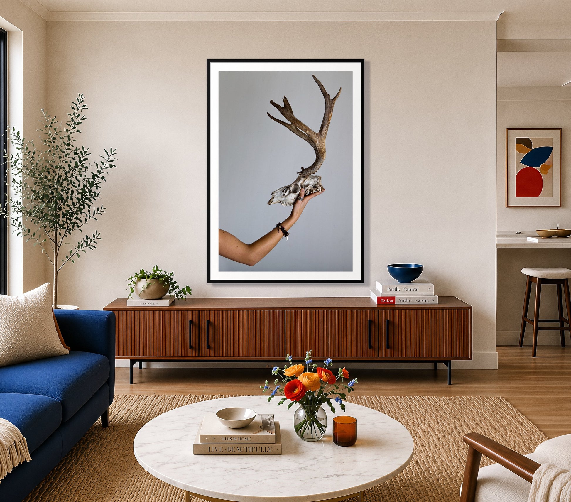 First Kill by Dylan Ozanich in a Black frame, above a walnut credenza in a bright living room with a blue sofa