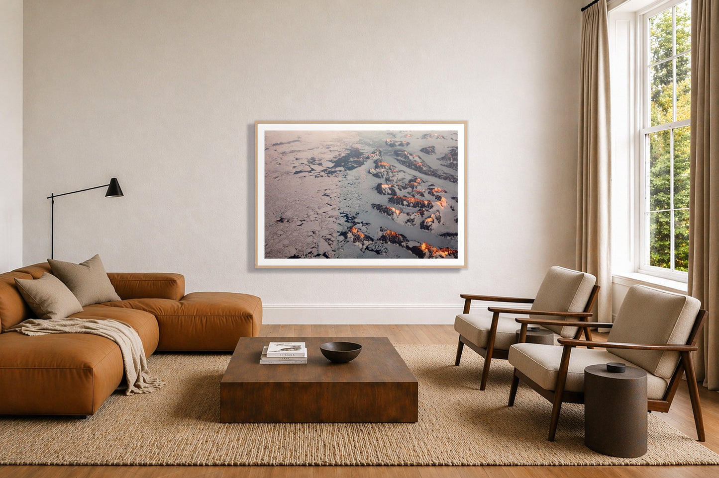 Greenland Peaks by Dylan Ozanich in an Oak frame, above a tan modular leather sofa in a minimal, sunlit living room