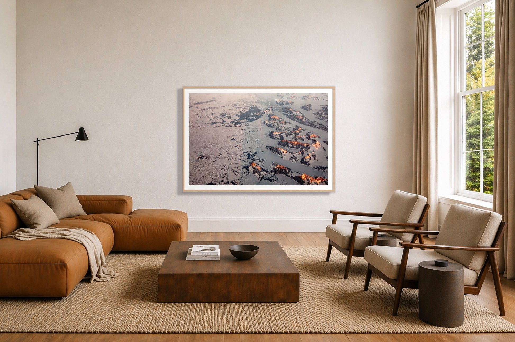 Greenland Peaks by Dylan Ozanich in an Oak frame, above a tan modular leather sofa in a minimal, sunlit living room