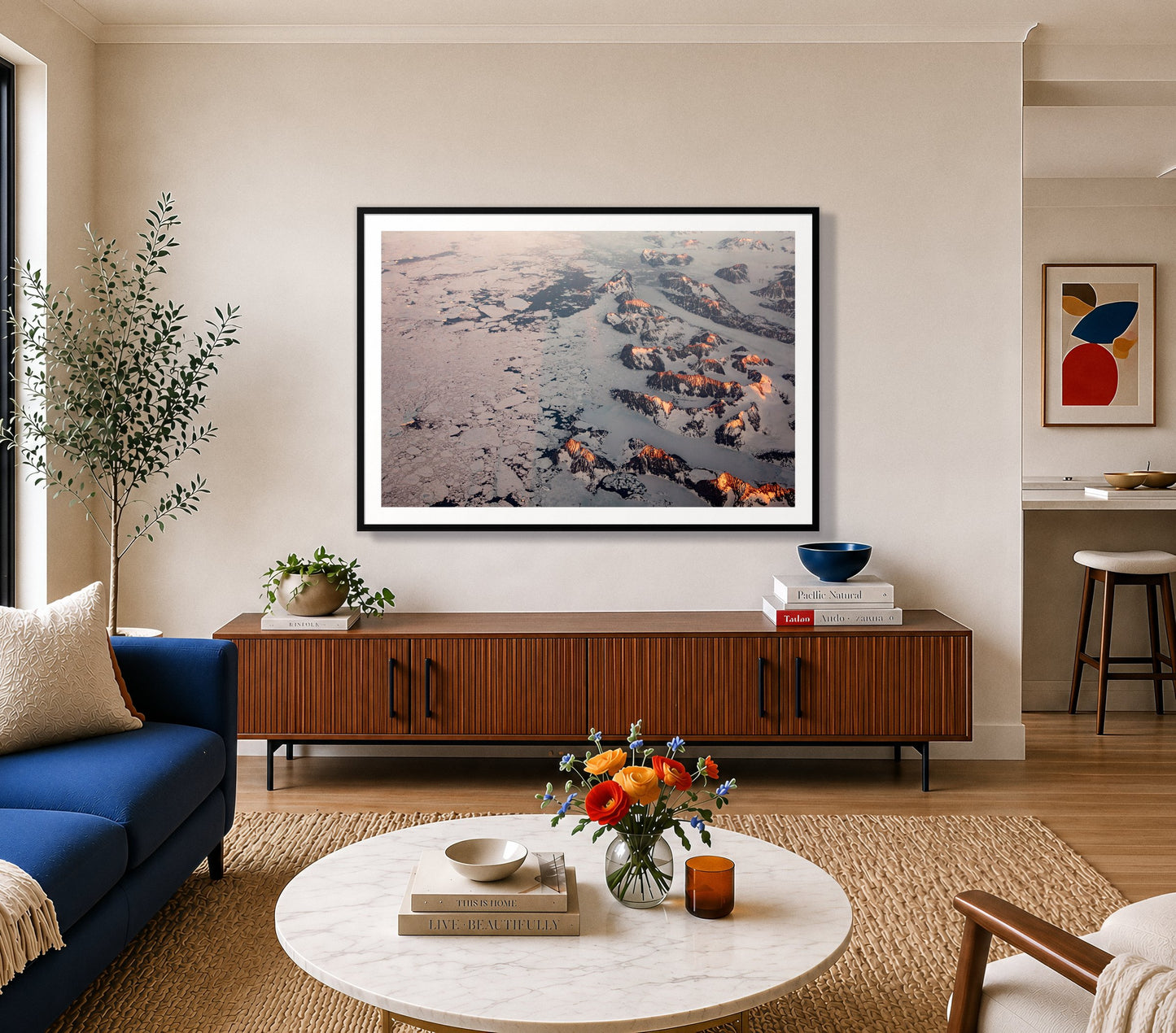 Greenland Peaks by Dylan Ozanich in a Black frame, above a walnut credenza in a bright living room with a blue sofa