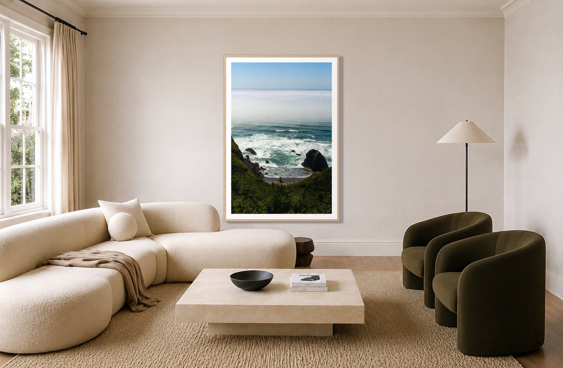 Oregon Coast by Dylan Ozanich in an Oak frame, above a cream curved sofa in a living room with olive velvet armchairs