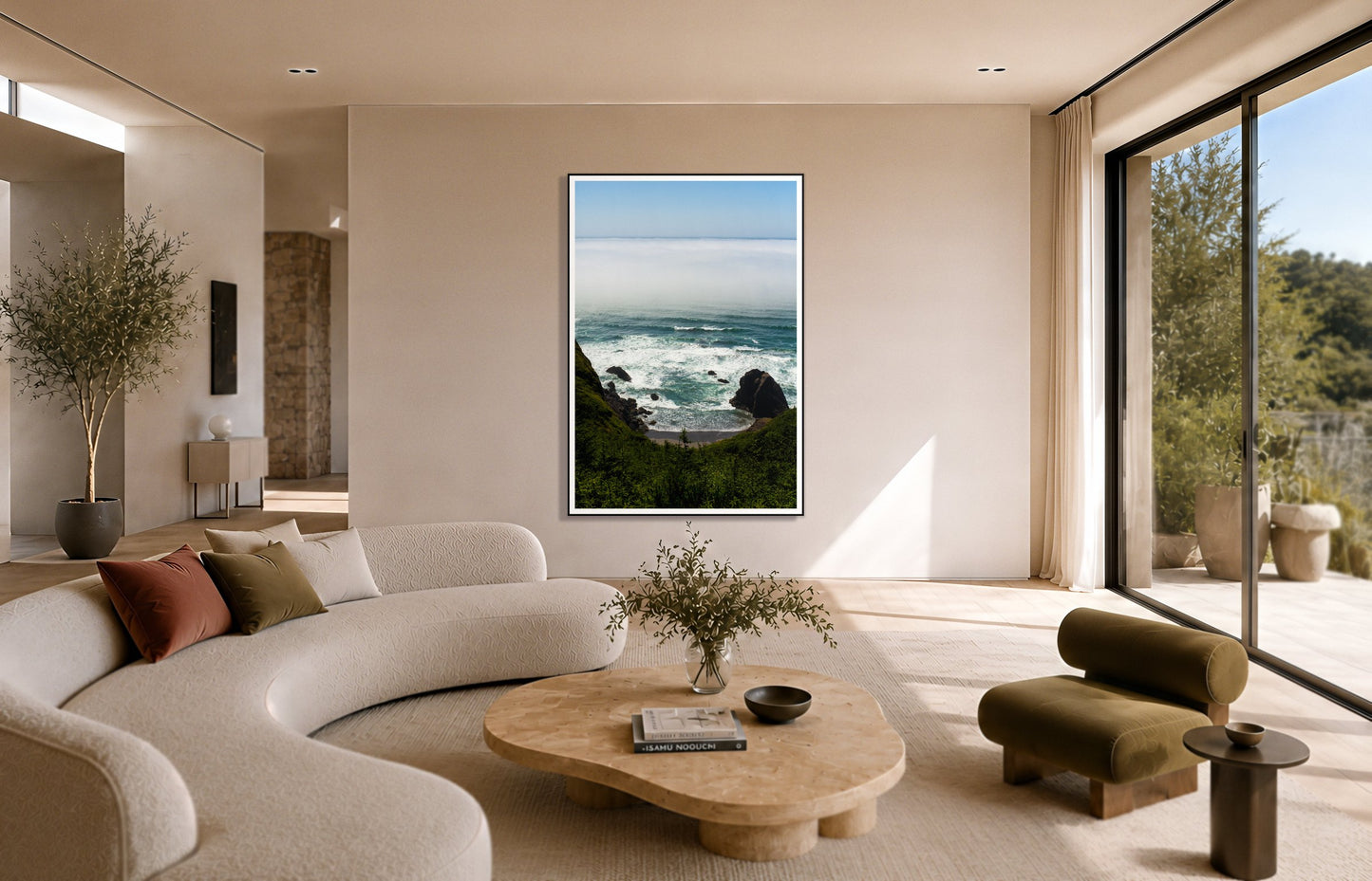 Oregon Coast by Dylan Ozanich in a Black frame, above a cream curved sofa in a sunlit room with olive velvet seating