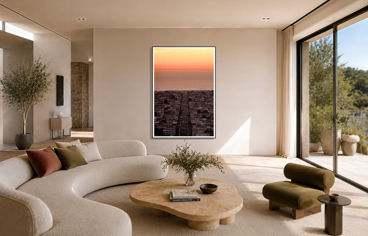 Sunset Streets by Dylan Ozanich in a Black frame, above a cream curved sofa in a sunlit room with olive velvet seating
