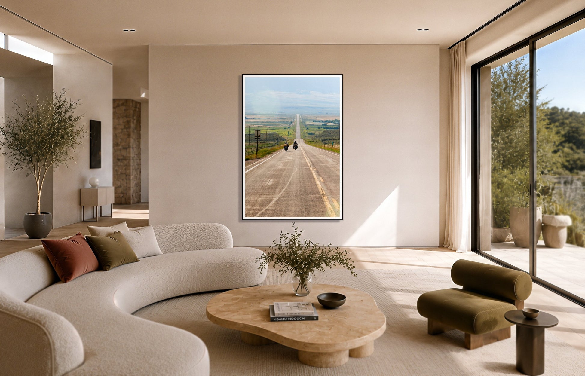 The Long Road by Dylan Ozanich in a Black frame, above a cream curved sofa in a sunlit room with olive velvet seating